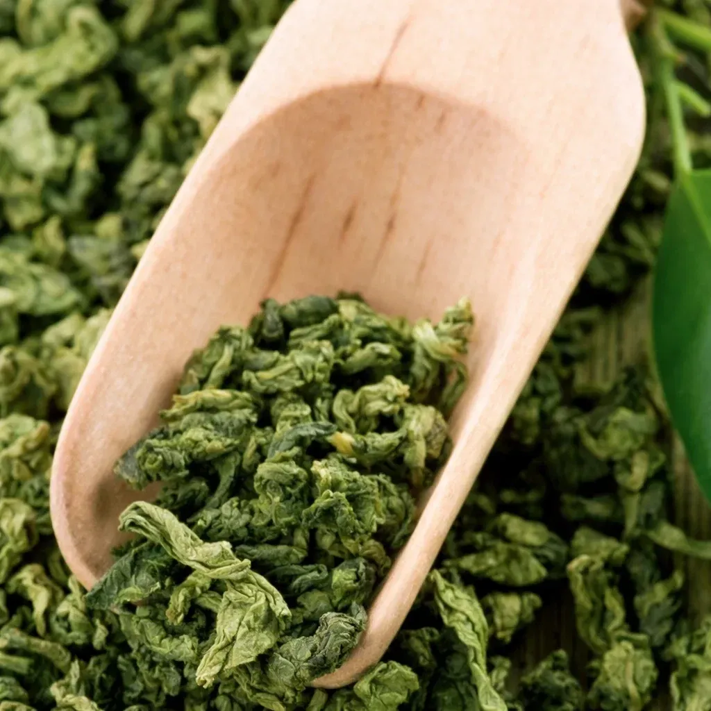 Loose green tea leaves in a wooden scoop, a natural source of L-theanine